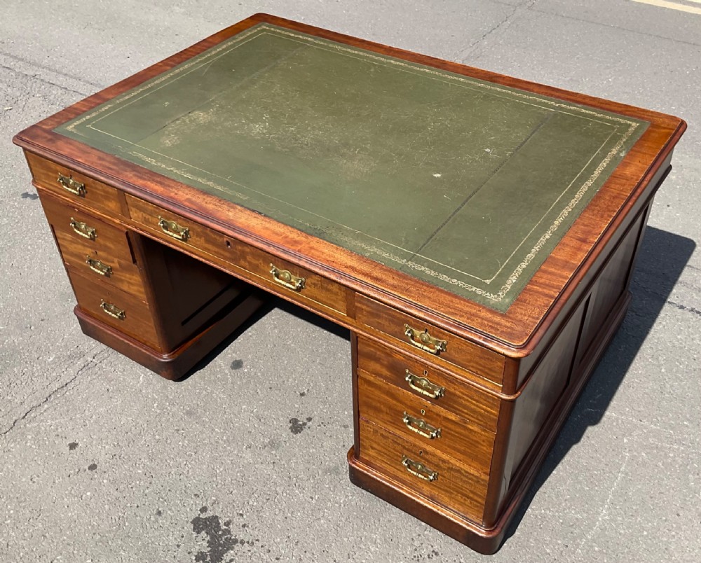 A Victorian mahogany pedestal desk featuring a green leather inset writing surface, nine drawers with brass handles, and twin pedestal bases. View VII