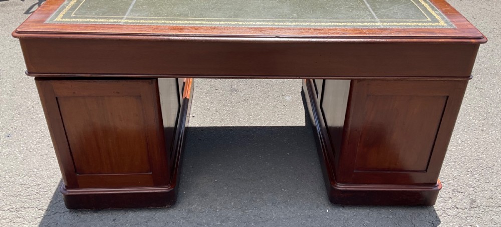 A Victorian mahogany pedestal desk featuring a green leather inset writing surface, nine drawers with brass handles, and twin pedestal bases. View VIII