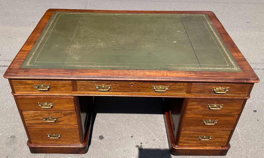 A Victorian mahogany pedestal desk featuring a green leather inset writing surface, nine drawers with brass handles, and twin pedestal bases. View IX