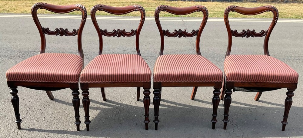 A set of four Victorian rosewood dining chairs featuring carved balloon backs, striped fabric upholstery, and turned front legs.