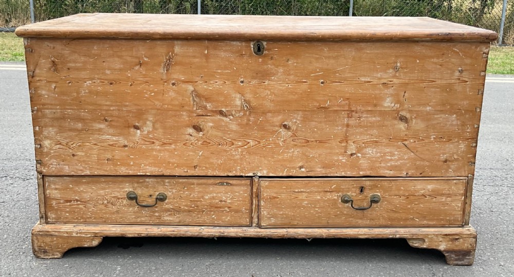 A large Georgian pine mule chest featuring a lift-top storage section above two lower drawers with brass drop handles and bracket feet.