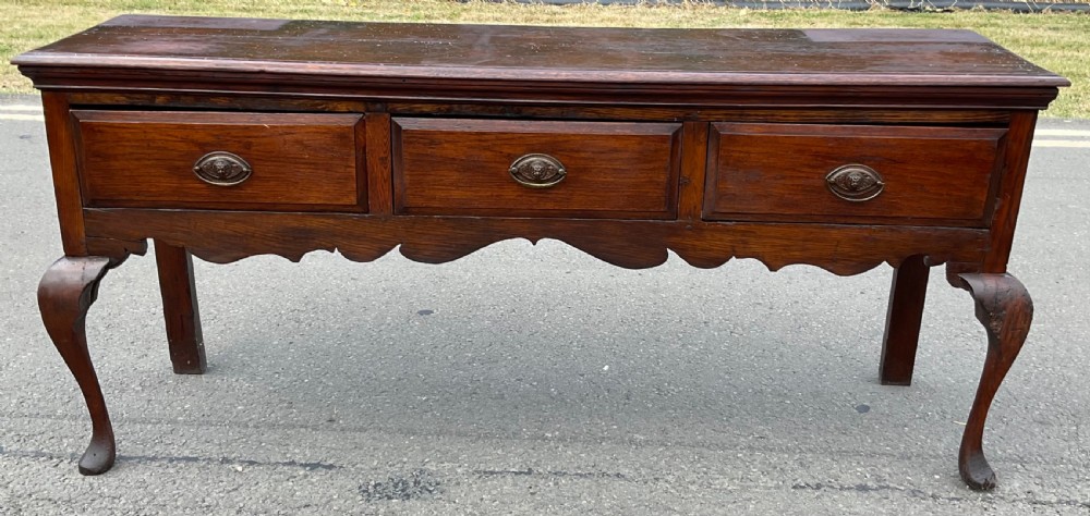 A Georgian dark oak dresser base featuring three drawers with oval brass handles, a shaped apron, and front cabriole legs. View II