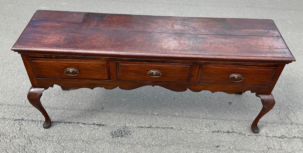 A Georgian dark oak dresser base featuring three drawers with oval brass handles, a shaped apron, and front cabriole legs. View IX