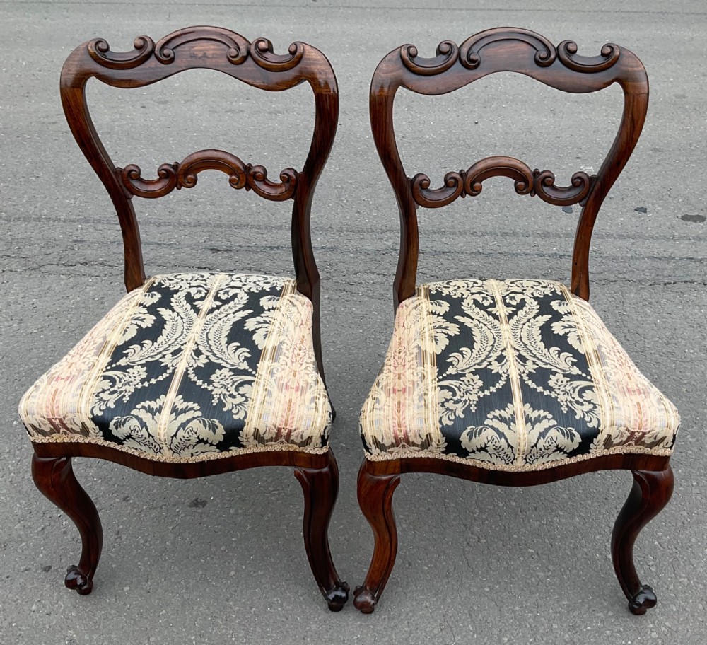 A pair of antique Victorian balloon back dining chairs crafted from dark rosewood with carved openwork backrests and patterned damask seats.