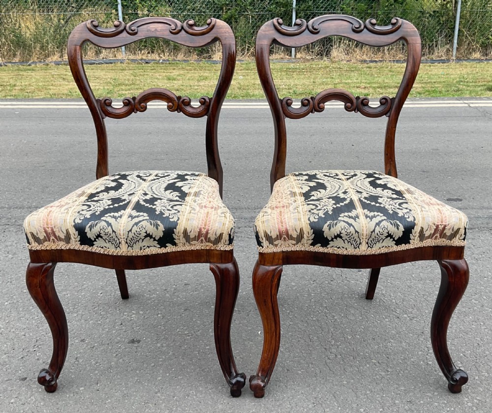 A pair of antique Victorian balloon back dining chairs crafted from dark rosewood with carved openwork backrests and patterned damask seats. View II