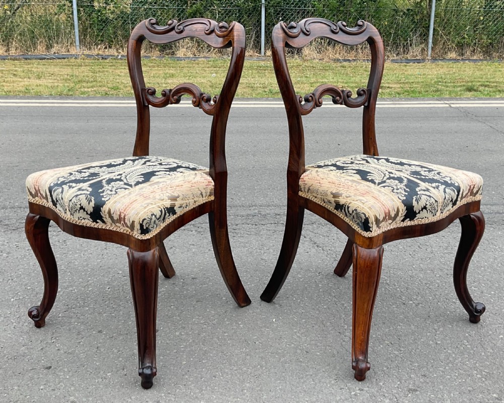 A pair of antique Victorian balloon back dining chairs crafted from dark rosewood with carved openwork backrests and patterned damask seats. View III