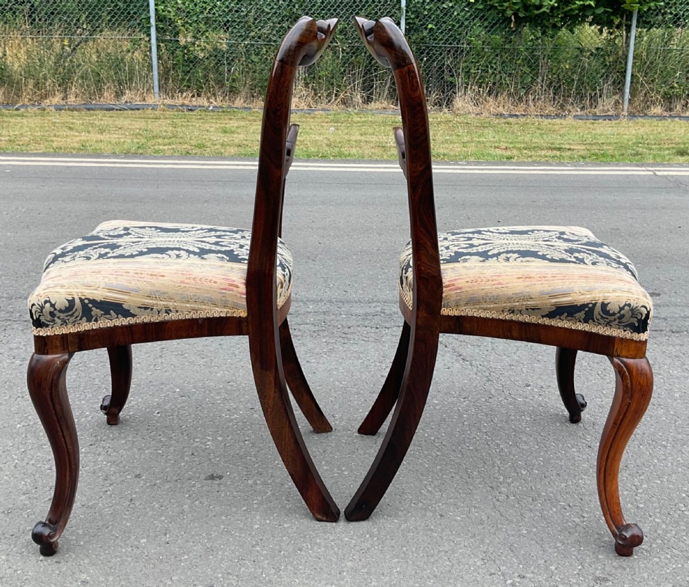 A pair of antique Victorian balloon back dining chairs crafted from dark rosewood with carved openwork backrests and patterned damask seats. View V