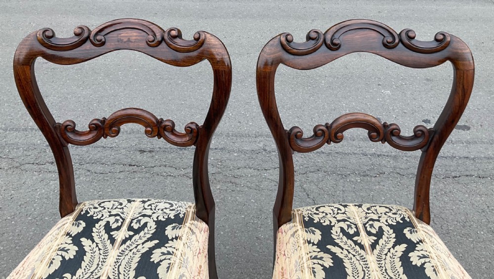 A pair of antique Victorian balloon back dining chairs crafted from dark rosewood with carved openwork backrests and patterned damask seats. View VI