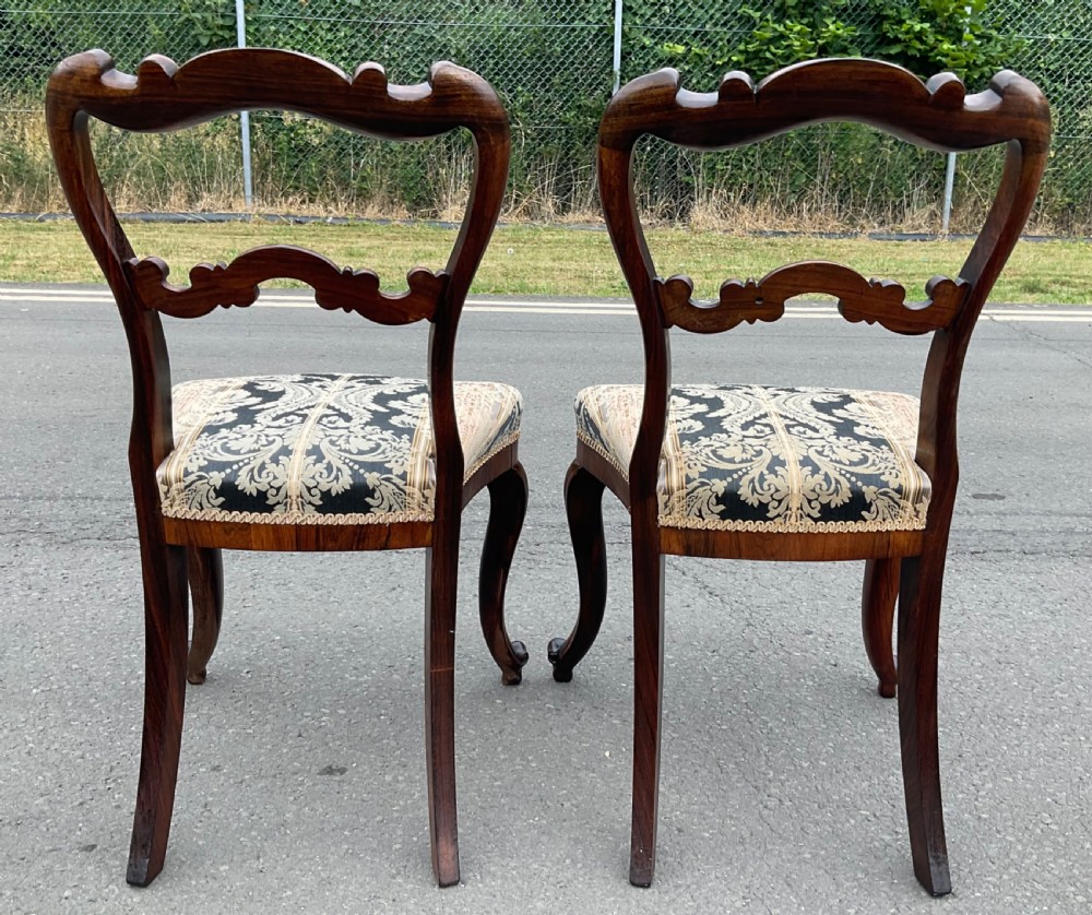 A pair of antique Victorian balloon back dining chairs crafted from dark rosewood with carved openwork backrests and patterned damask seats. View VII