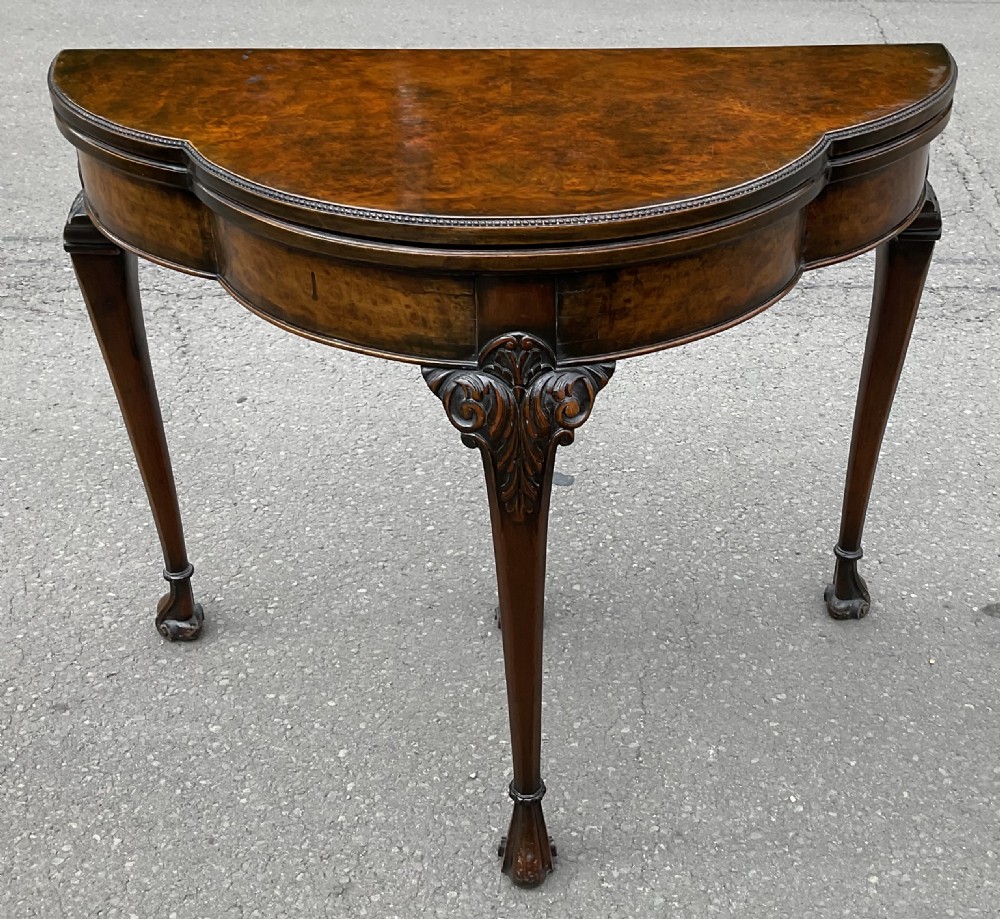 A Queen Anne style walnut foldover card table featuring a shaped top, carved cabriole legs, and claw and ball feet.