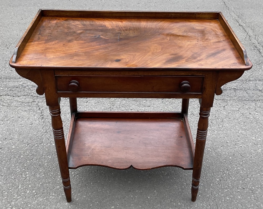A Victorian mahogany side table featuring a galleried top, single drawer with wooden knobs, turned legs, and a scalloped lower shelf.