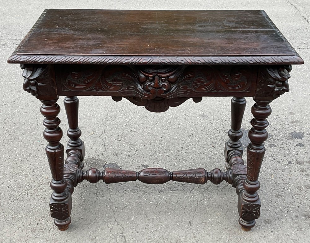 A dark brown Victorian carved oak side table featuring intricate mask carvings on the frieze, turned legs, and a carved lower stretcher.
