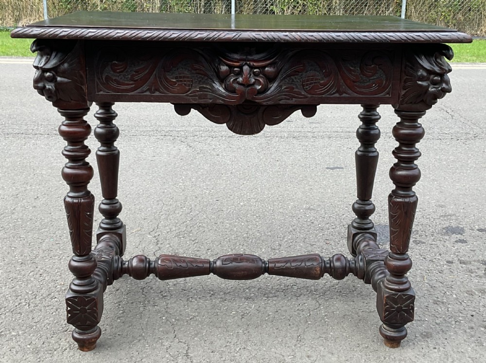 A dark brown Victorian carved oak side table featuring intricate mask carvings on the frieze, turned legs, and a carved lower stretcher. View II