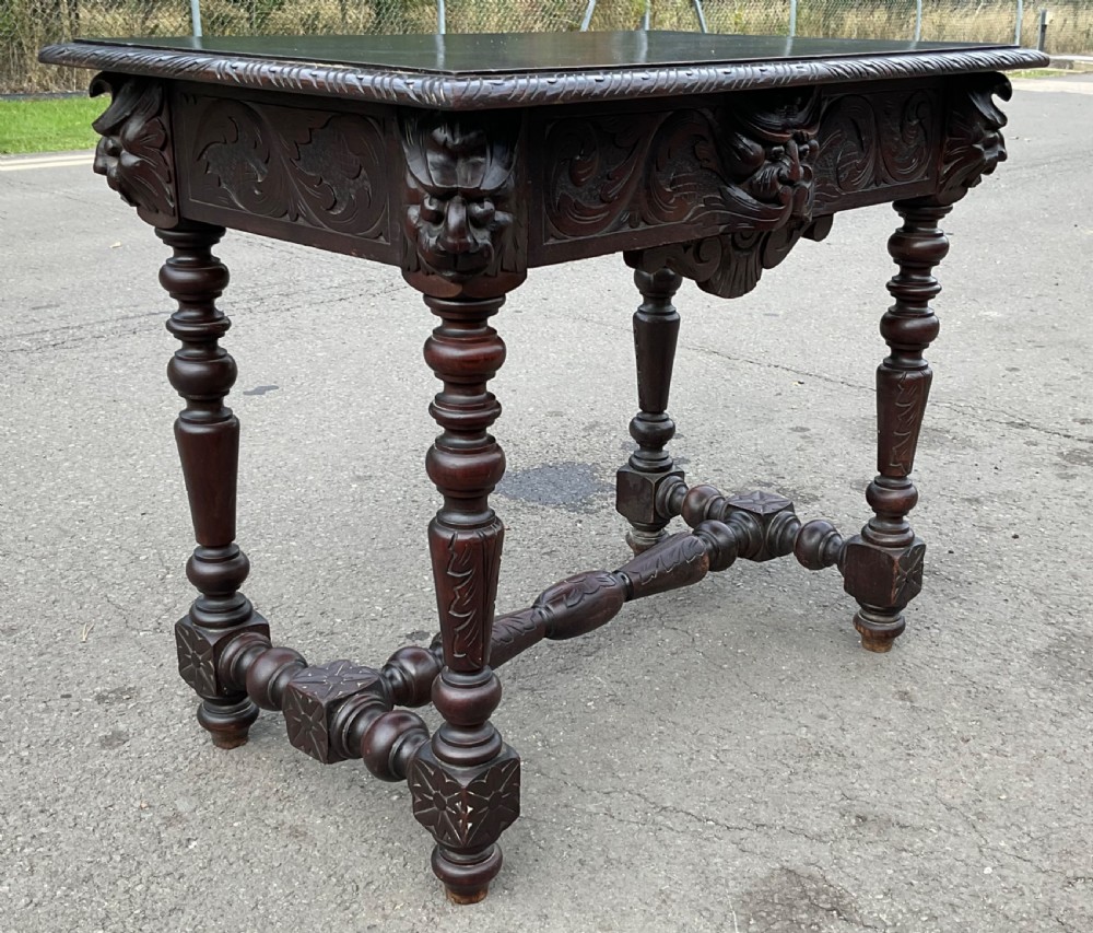 A dark brown Victorian carved oak side table featuring intricate mask carvings on the frieze, turned legs, and a carved lower stretcher. View III
