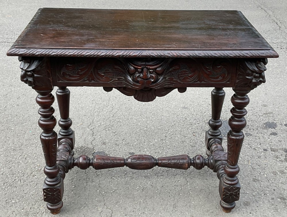 A dark brown Victorian carved oak side table featuring intricate mask carvings on the frieze, turned legs, and a carved lower stretcher. View IV