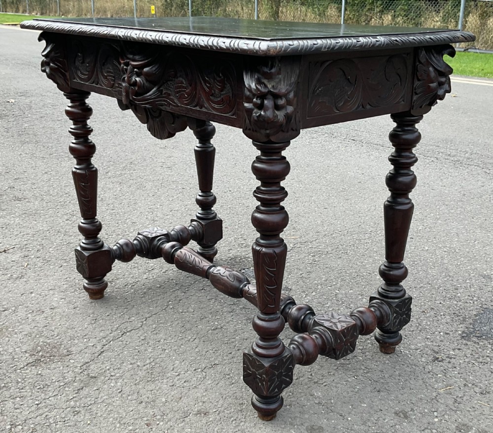A dark brown Victorian carved oak side table featuring intricate mask carvings on the frieze, turned legs, and a carved lower stretcher. View V