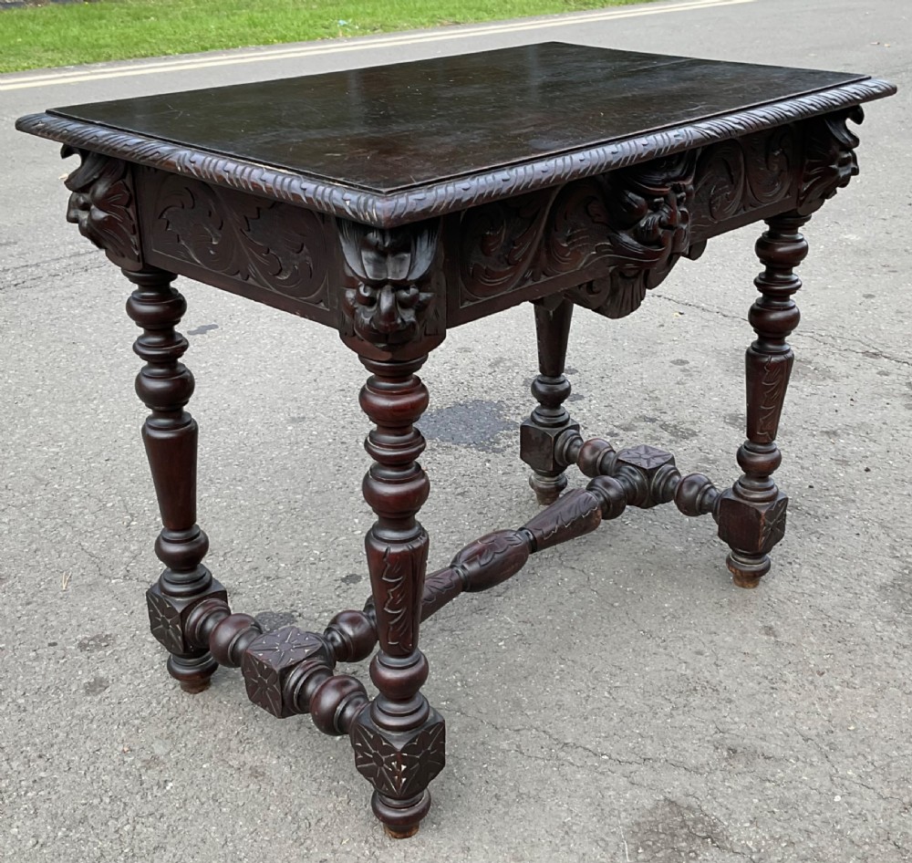 A dark brown Victorian carved oak side table featuring intricate mask carvings on the frieze, turned legs, and a carved lower stretcher. View VI