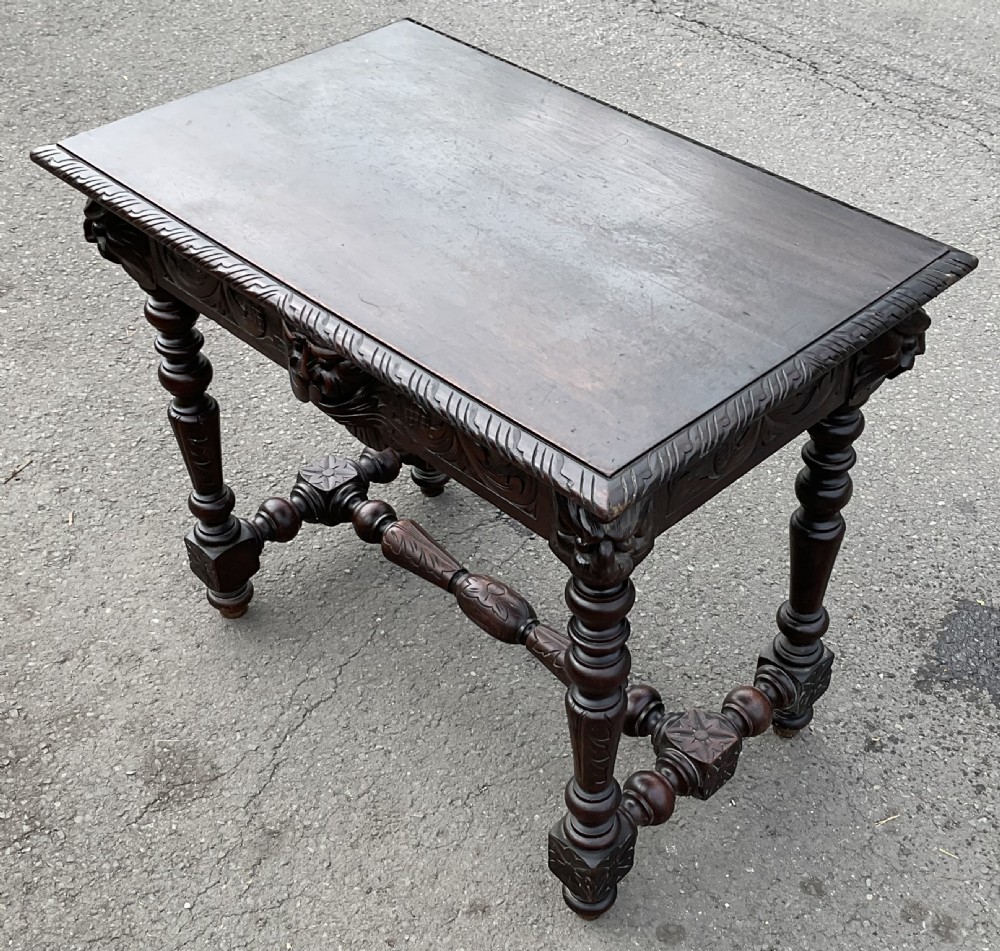 A dark brown Victorian carved oak side table featuring intricate mask carvings on the frieze, turned legs, and a carved lower stretcher. View VII