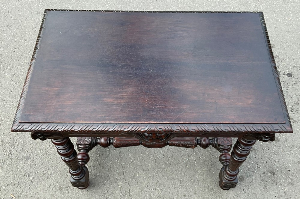 A dark brown Victorian carved oak side table featuring intricate mask carvings on the frieze, turned legs, and a carved lower stretcher. View VIII