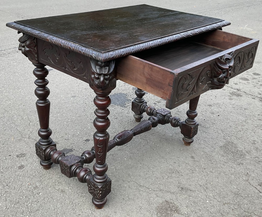 A dark brown Victorian carved oak side table featuring intricate mask carvings on the frieze, turned legs, and a carved lower stretcher. View X