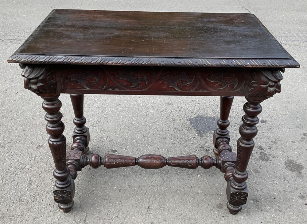 A dark brown Victorian carved oak side table featuring intricate mask carvings on the frieze, turned legs, and a carved lower stretcher. View XI