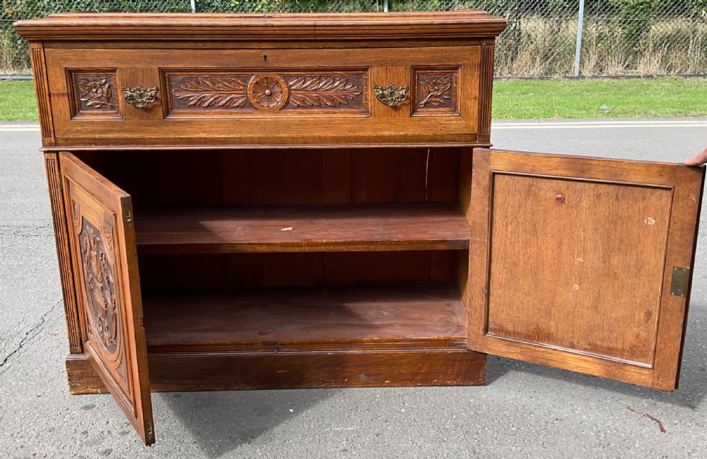 An Edwardian oak secretaire bookcase featuring a glazed upper display cabinet, a carved middle drawer with brass handles, and carved double cupboard doors below. View VIII