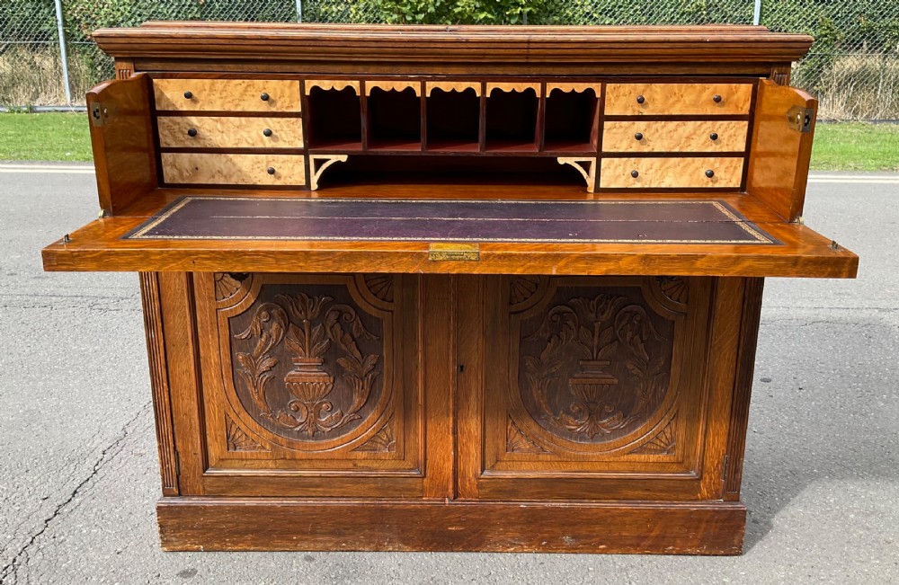 An Edwardian oak secretaire bookcase featuring a glazed upper display cabinet, a carved middle drawer with brass handles, and carved double cupboard doors below. View IX