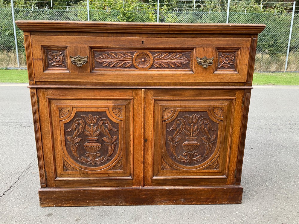 An Edwardian oak secretaire bookcase featuring a glazed upper display cabinet, a carved middle drawer with brass handles, and carved double cupboard doors below. View X