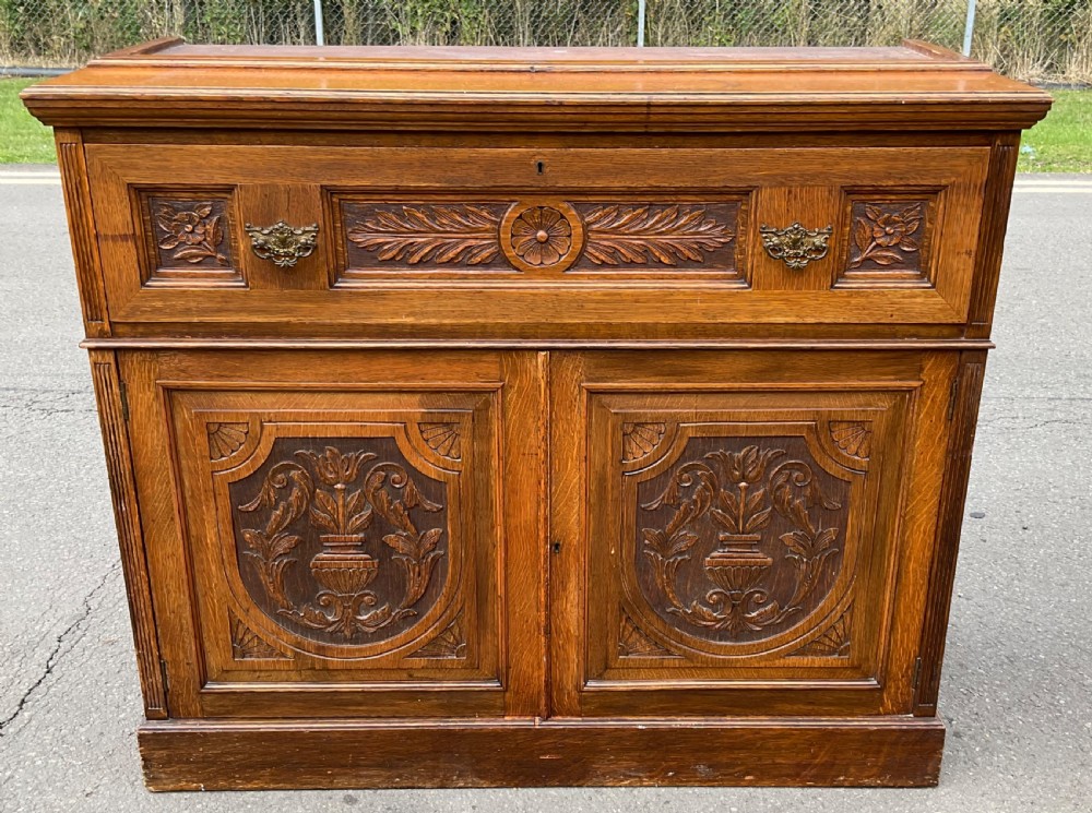 An Edwardian oak secretaire bookcase featuring a glazed upper display cabinet, a carved middle drawer with brass handles, and carved double cupboard doors below. View XI