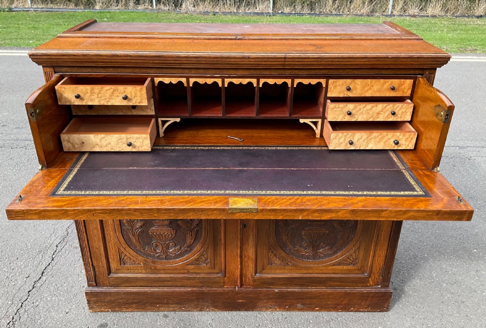 An Edwardian oak secretaire bookcase featuring a glazed upper display cabinet, a carved middle drawer with brass handles, and carved double cupboard doors below. View XII