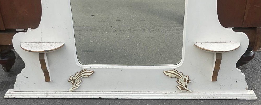 An Edwardian cream painted overmantel mirror with an arched glass centre, carved gold accent flourishes, and two small side display shelves. View III