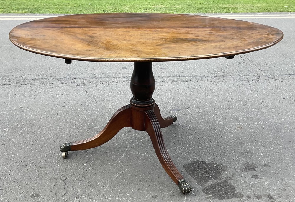 An antique Georgian oval mahogany breakfast table featuring a central turned pedestal column and four reeded legs with brass castors.