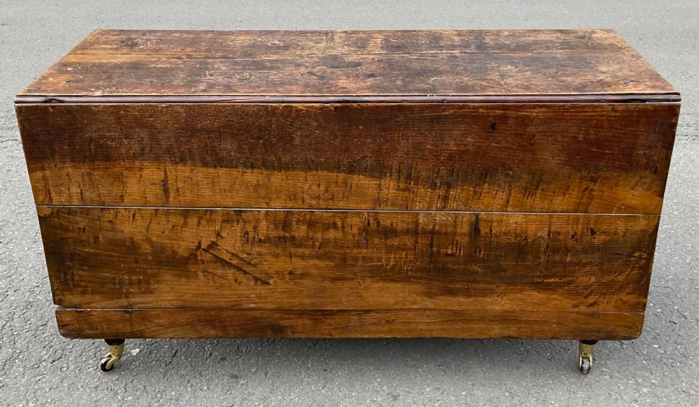 A closed Georgian solid oak drop-leaf dining table featuring a textured brown wood grain finish and brass castors.
