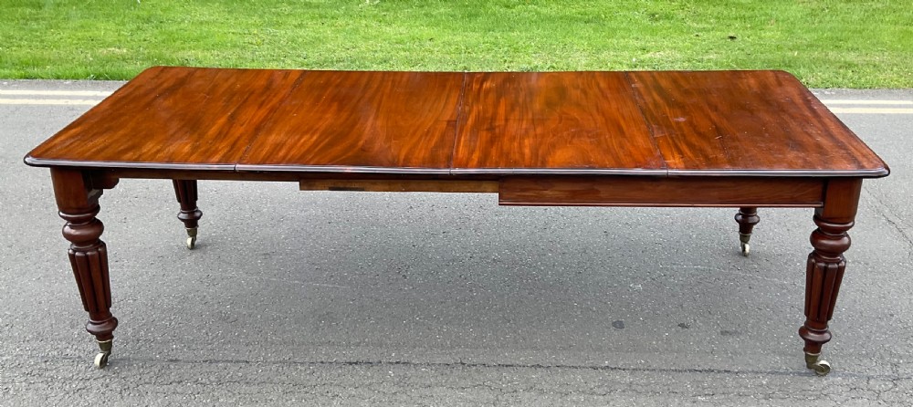 A large William IV mahogany extending dining table with a rectangular top, rounded corners, and reeded turned legs on brass castors.