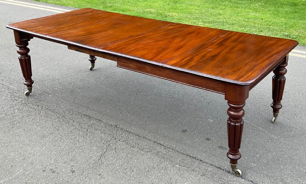 A large William IV mahogany extending dining table with a rectangular top, rounded corners, and reeded turned legs on brass castors. View II