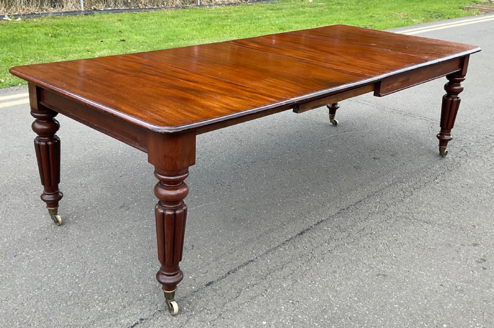 A large William IV mahogany extending dining table with a rectangular top, rounded corners, and reeded turned legs on brass castors. View III