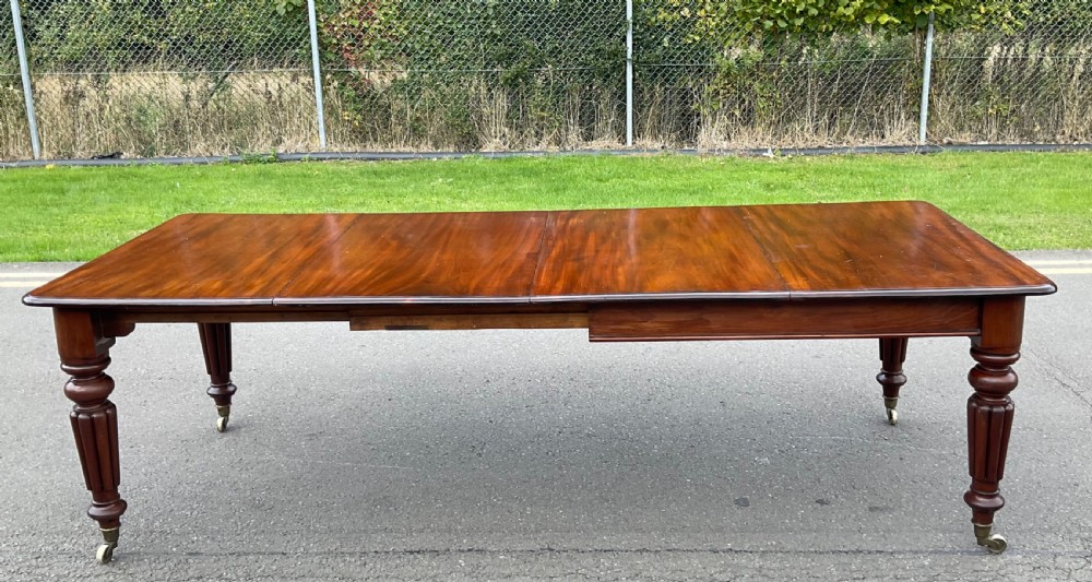 A large William IV mahogany extending dining table with a rectangular top, rounded corners, and reeded turned legs on brass castors. View V