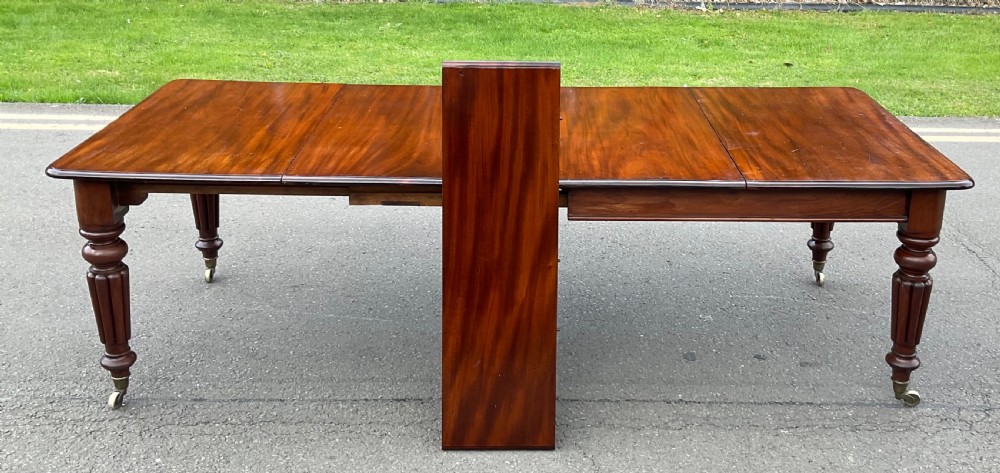 A large William IV mahogany extending dining table with a rectangular top, rounded corners, and reeded turned legs on brass castors. View VI