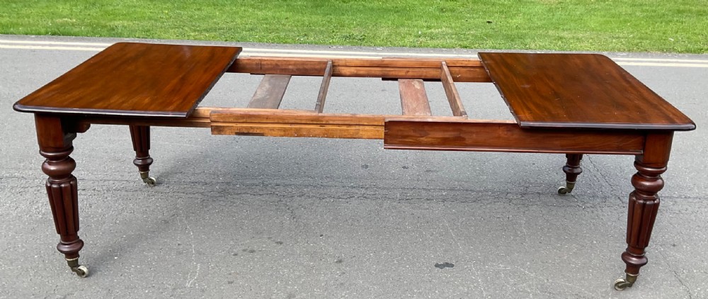 A large William IV mahogany extending dining table with a rectangular top, rounded corners, and reeded turned legs on brass castors. View VII