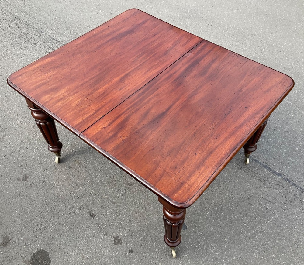 A large William IV mahogany extending dining table with a rectangular top, rounded corners, and reeded turned legs on brass castors. View VIII