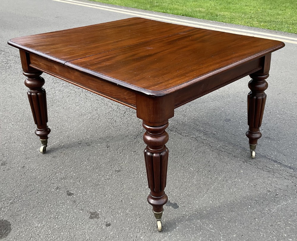 A large William IV mahogany extending dining table with a rectangular top, rounded corners, and reeded turned legs on brass castors. View IX