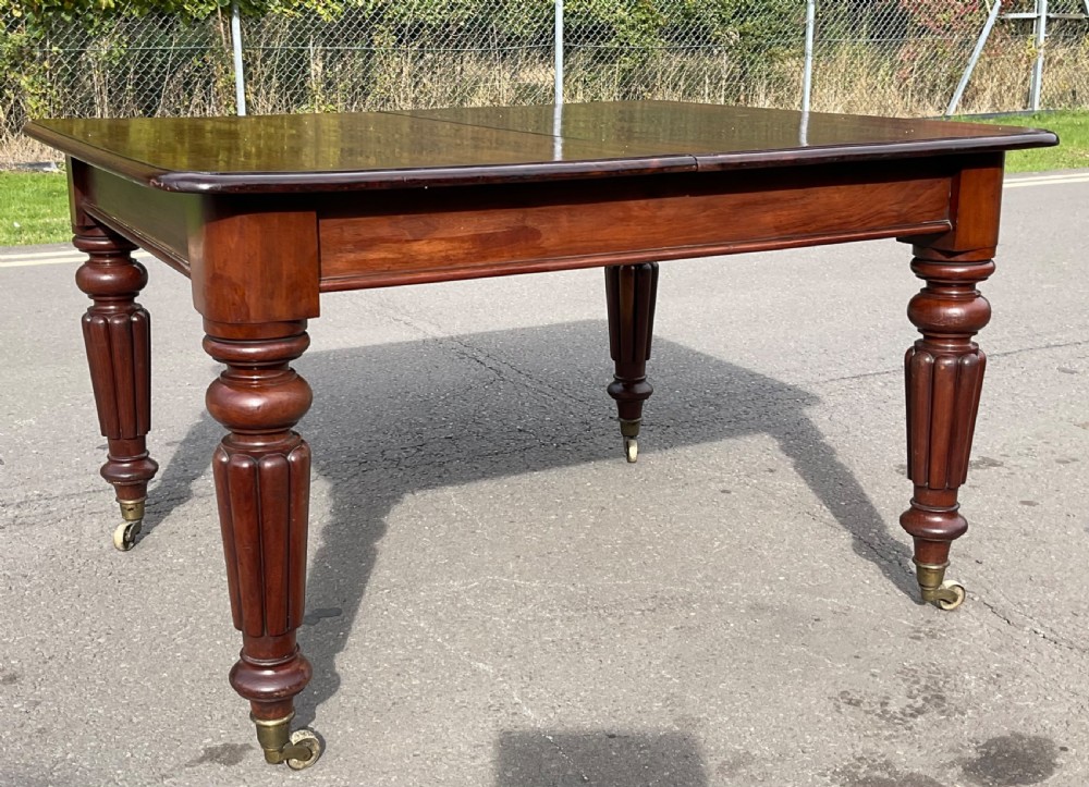 A large William IV mahogany extending dining table with a rectangular top, rounded corners, and reeded turned legs on brass castors. View X