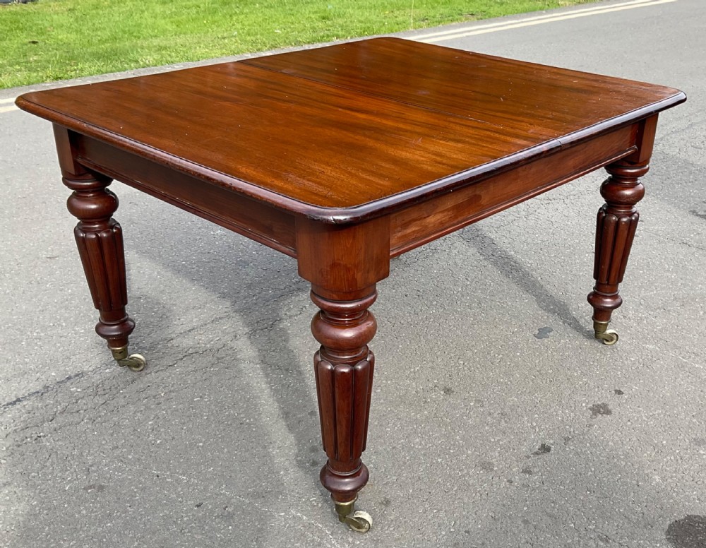 A large William IV mahogany extending dining table with a rectangular top, rounded corners, and reeded turned legs on brass castors. View XII