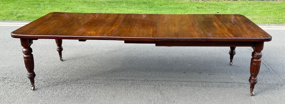 A long Victorian mahogany extending dining table with three insert leaves, rounded corners, and turned legs with brass castors.