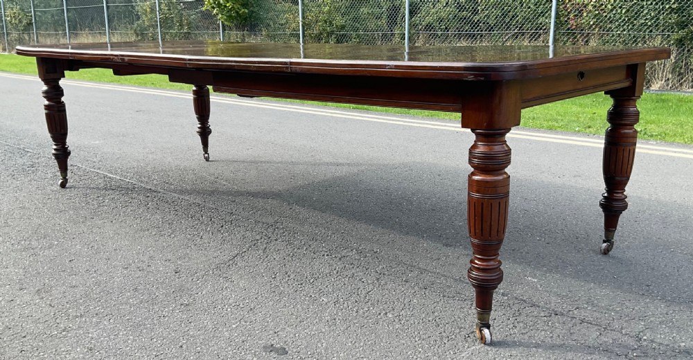 A long Victorian mahogany extending dining table with three insert leaves, rounded corners, and turned legs with brass castors. View II