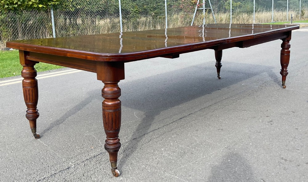 A long Victorian mahogany extending dining table with three insert leaves, rounded corners, and turned legs with brass castors. View V