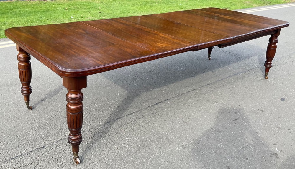 A long Victorian mahogany extending dining table with three insert leaves, rounded corners, and turned legs with brass castors. View VI