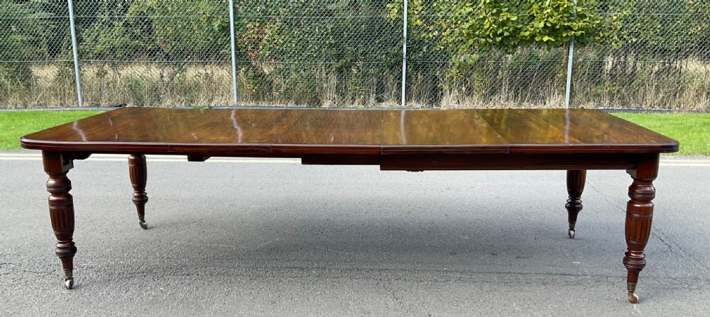 A long Victorian mahogany extending dining table with three insert leaves, rounded corners, and turned legs with brass castors. View VII