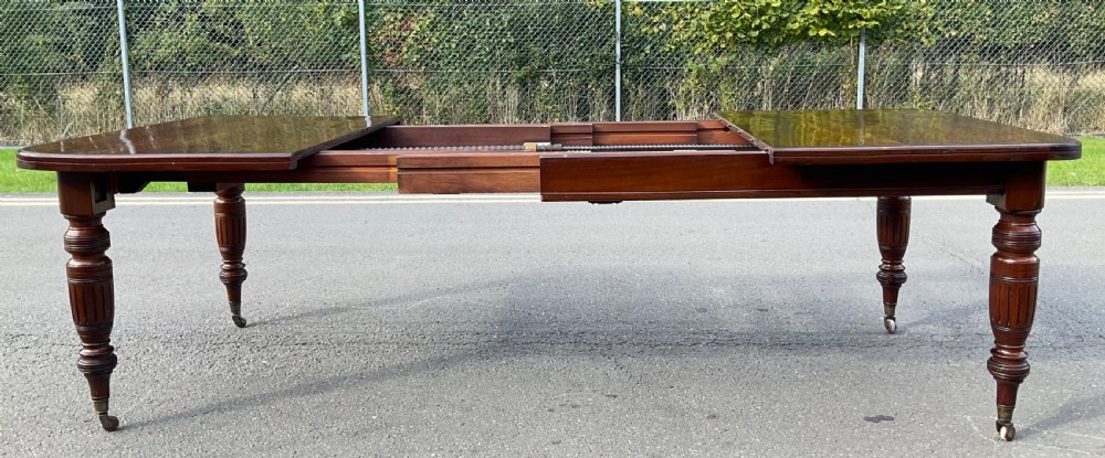 A long Victorian mahogany extending dining table with three insert leaves, rounded corners, and turned legs with brass castors. View VIII