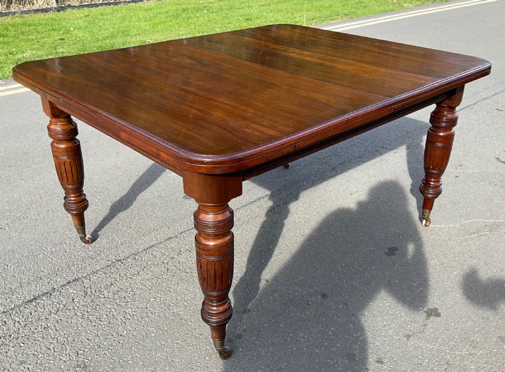 A long Victorian mahogany extending dining table with three insert leaves, rounded corners, and turned legs with brass castors. View IX